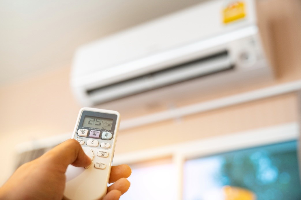 A person holding a remote in front of an air conditioner.
